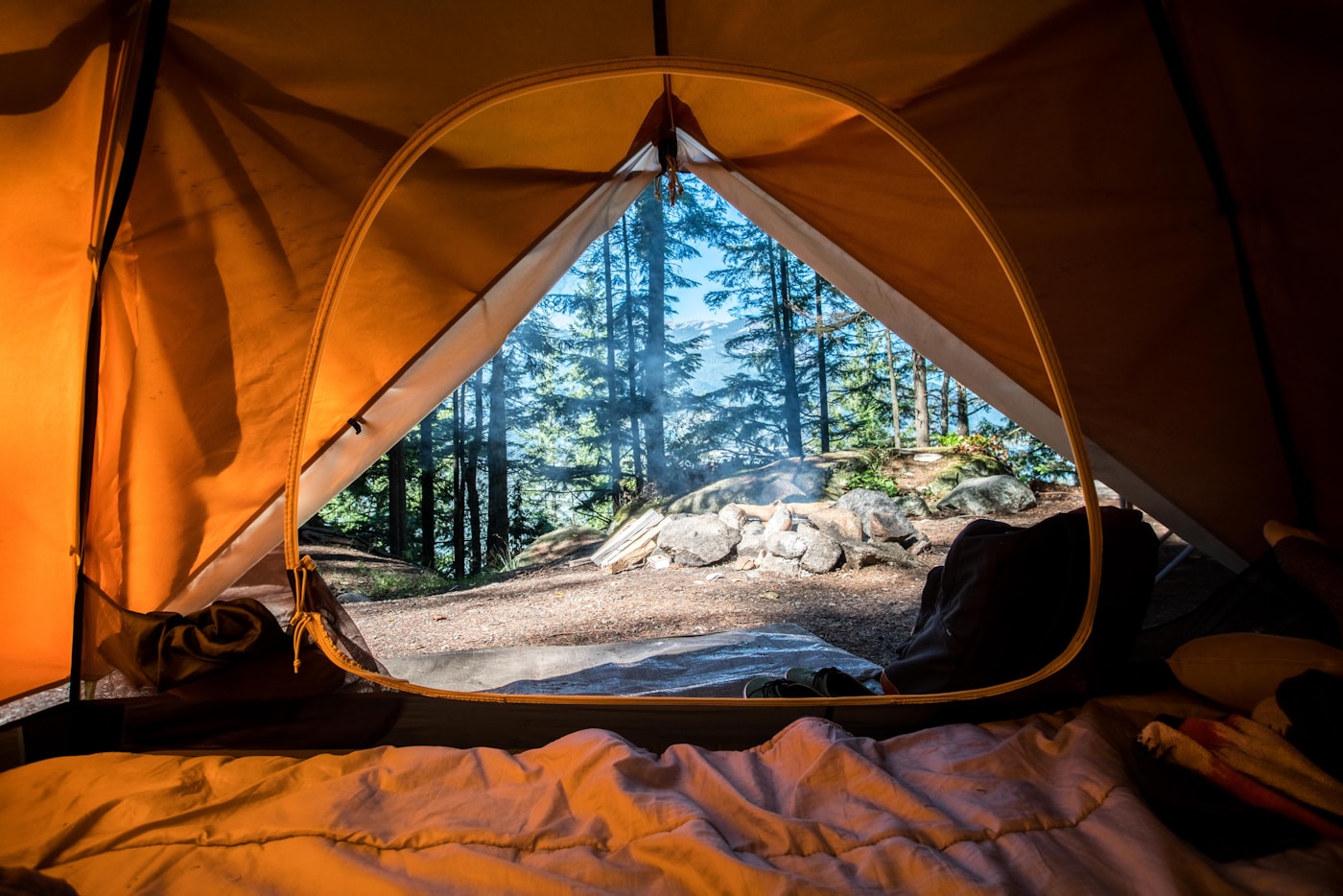 Canvas tent and campfire under trees — classic summer camp setting
